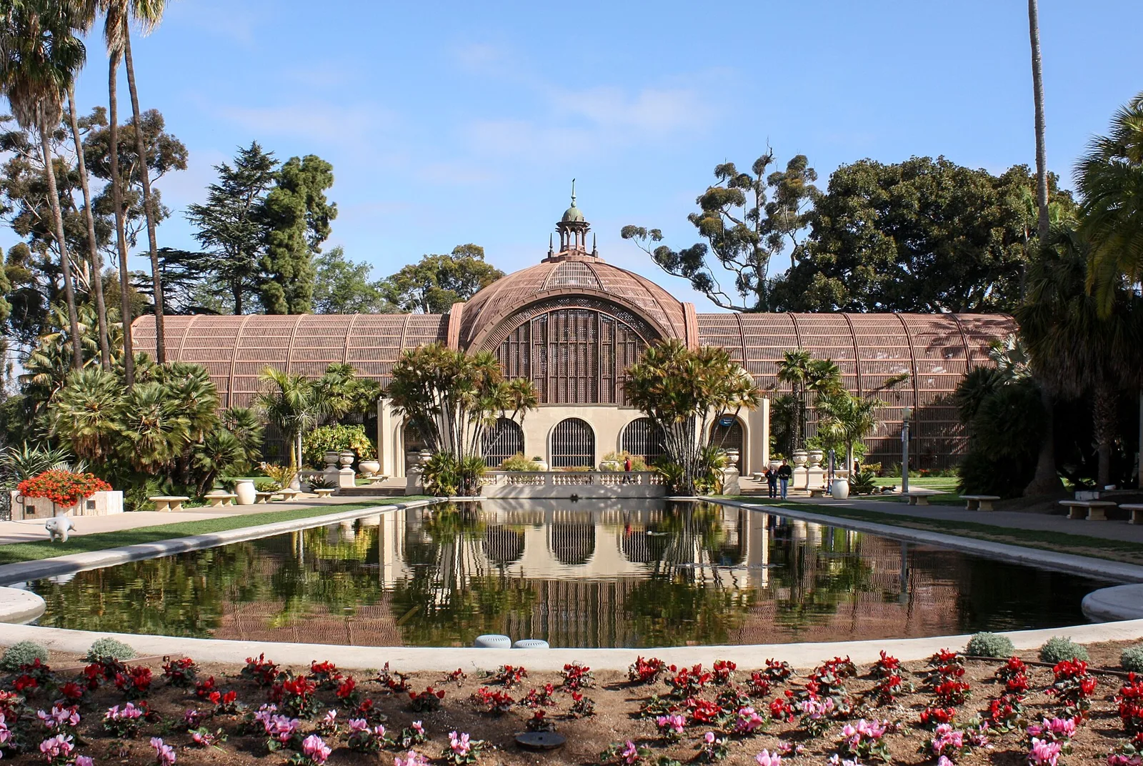 The domed wooden lath Botanical Building reflected in the long Lily Pond, framed by palms and flower beds in Balboa Park